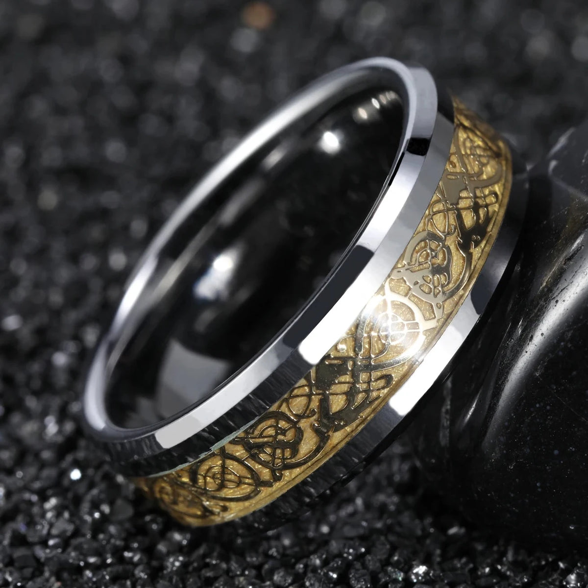 A silver-toned metal ring with an intricate gold-toned engraved band, resting on a dark textured surface.